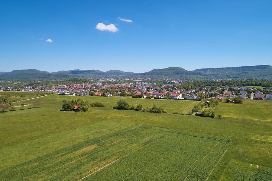 Luftbild einer großen Ortschaft, im Vordergrund Felder, im Hintergrund die Bergkette der Schwäbischen Alberg