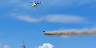Helikopter, darunter eine Art Staubfahne, über einem Baumwipfel