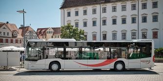 Bus mit dem geschwungenen Logo und Beschriftung kreisbus.de steht auf einem großen Platz, im Hintergrund Gebäude