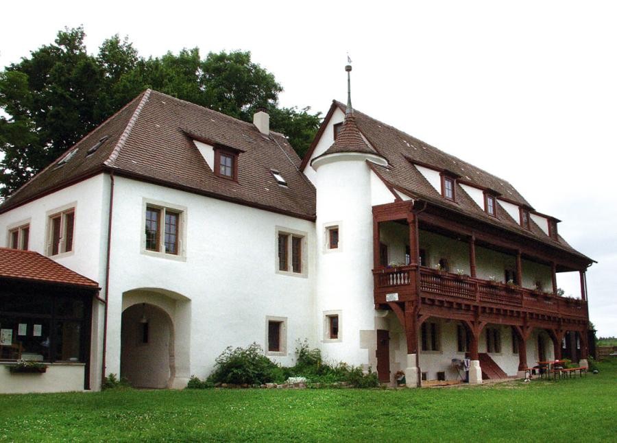 Zwei aneinandergebaute Schlossgebäude mit schlankem rundem Turm, das längliche zweite Gebäude hat vorgesetzt eine zweistöckige Holzgalerie