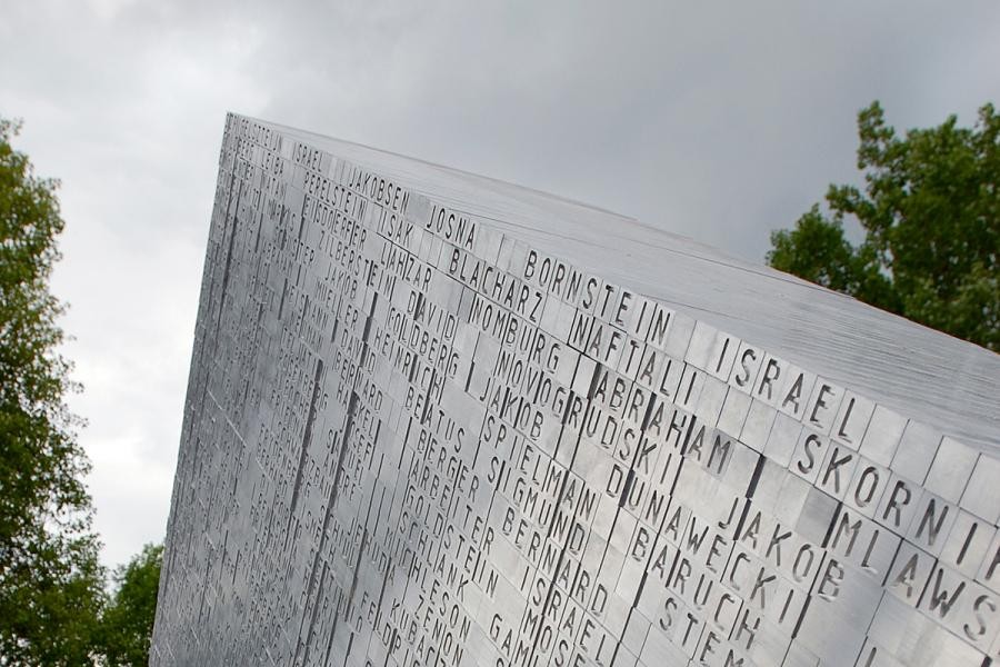 Teil des Denkmals: ein mit der Spitze nach oben zeigendes skulpturales Dreieck aus Aluminium, geformt aus einzelnen als unregelmäßige Oberfläche leicht abgesetzten Stiften mit Buchstaben die Namen ergeben 