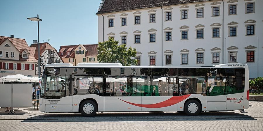 Bus mit dem geschwungenen Logo auf der Seite und Beschriftung "KREISBUS – der Bringer" auf einem großen Platz, Häuser im Hintergrund