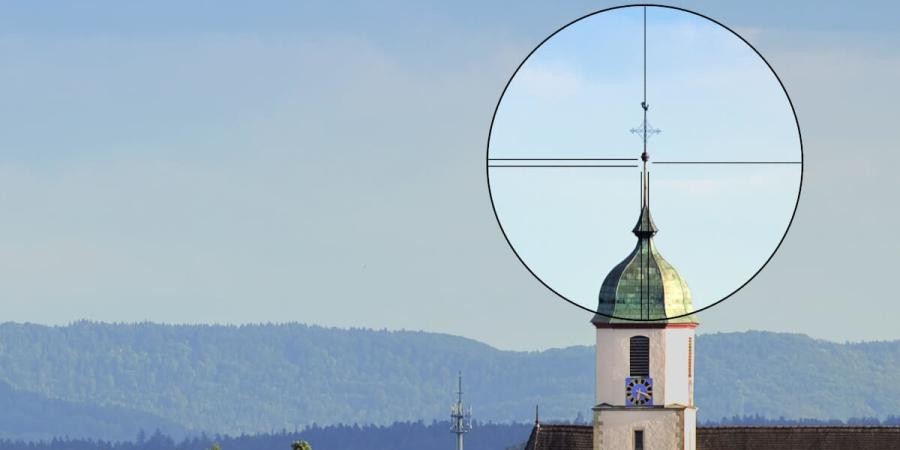 Das Bild zeigt einen Kirchturm. Um die Kirchturmspitze ist ein schwarz umrandeter Kreis mit verschiedenen Messlinien zu sehen. Im Hintergrund sind blauer Himmel und Wolken zu sehen. Im Hintergrund des Bildes sind Wälder zu erkennen.